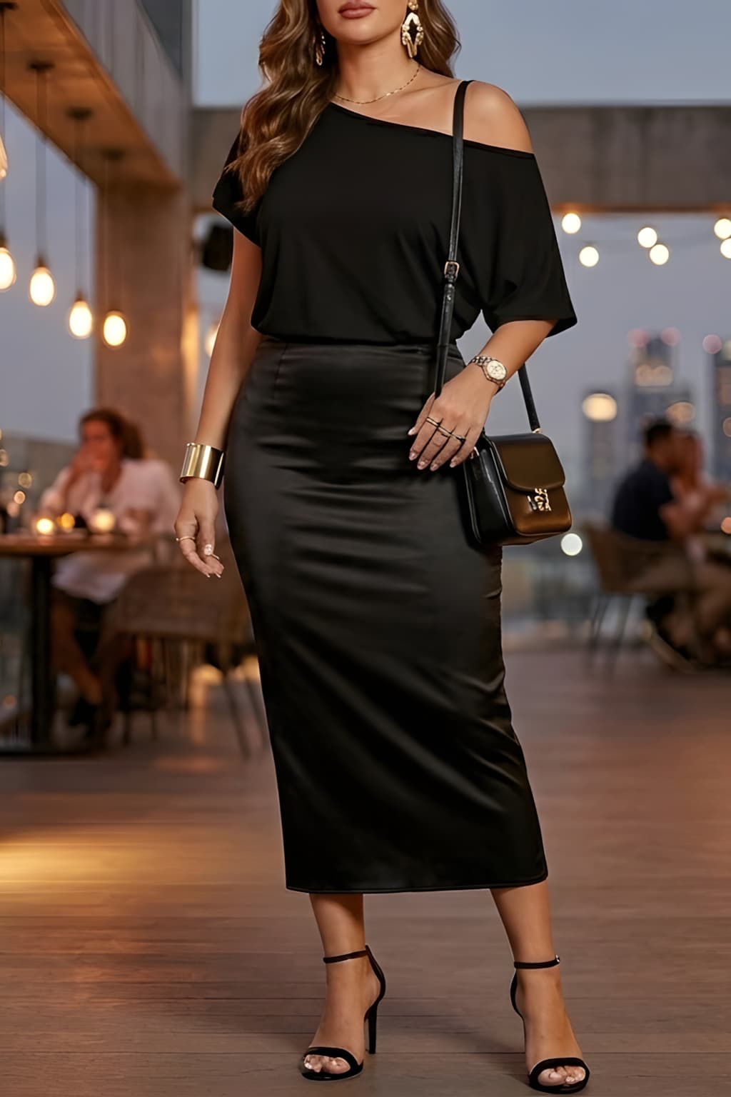 An American woman is in a chic feminine evening outfit style wearing a black off shoulder top from Amazon—she styles her outfit with a black satin midi skirt and strappy heels at a rooftop city restaurant.
