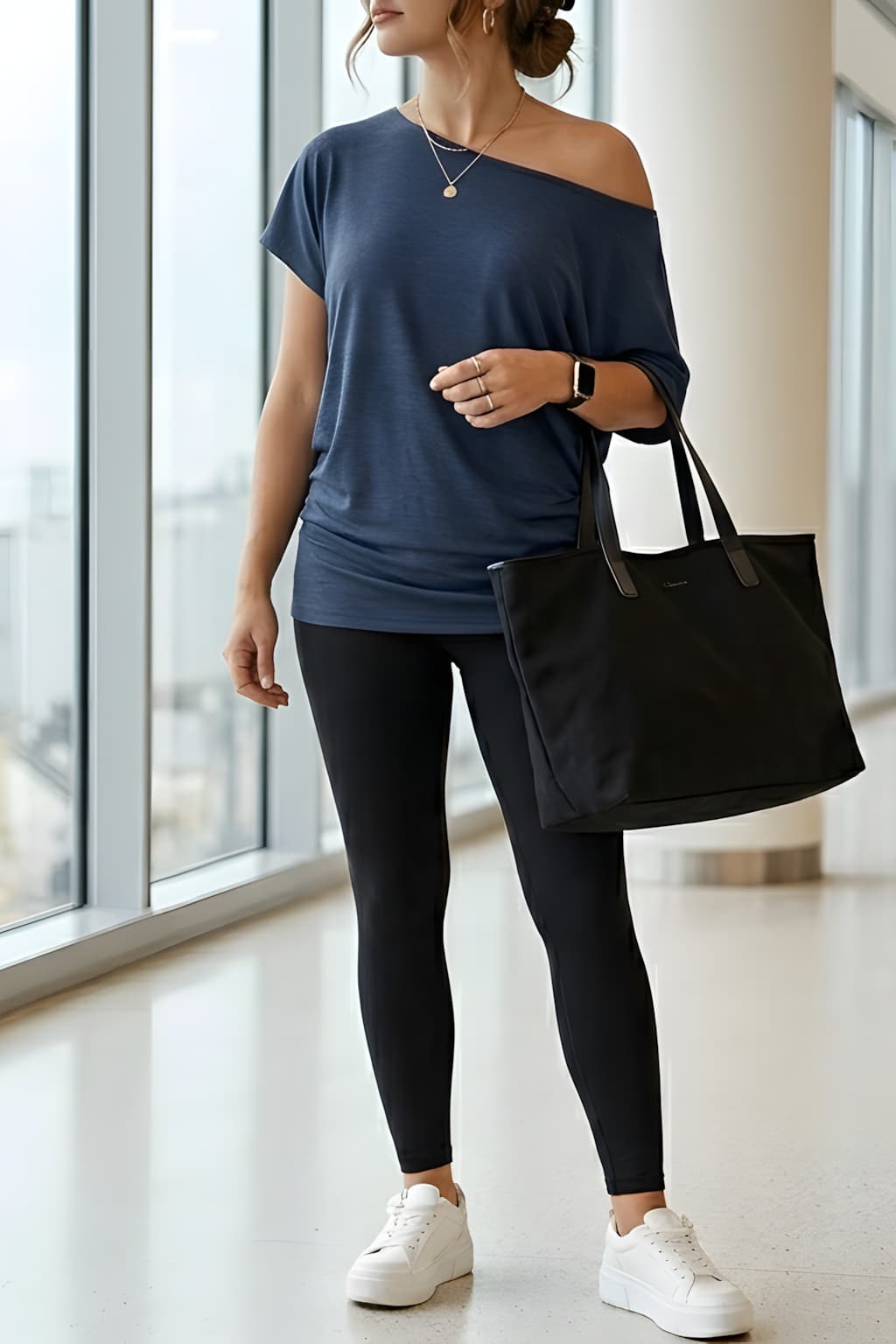 An American woman is in a clean chic travel outfit style wearing a navy off shoulder top from Amazon—she styles her outfit with black leggings and chunky white sneakers inside a modern airport terminal.